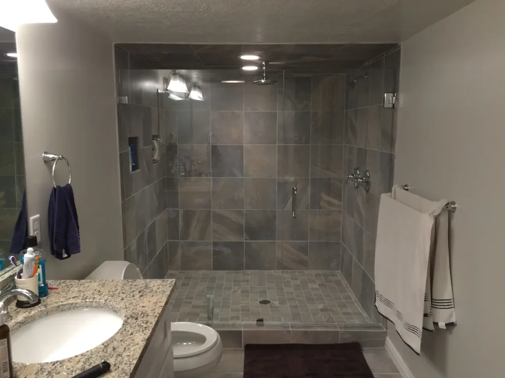 Modern basement bathroom with a large walk-in tile shower, frameless glass enclosure, gray tile walls, and recessed lighting.