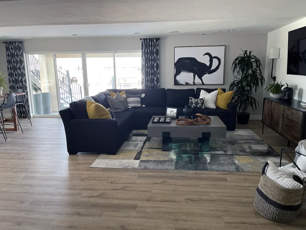 Finished basement living room with dark sectional seating, wood flooring, area rug, fireplace, and large windows providing natural light.