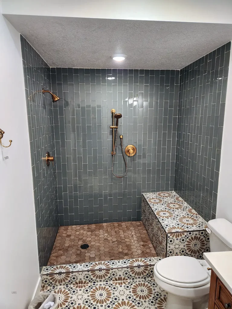 walk in basement shower with blue tile and brass fixtures and Eruo style glass door